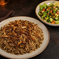 طبق مجدرة سورية بالعدس والأرز ومزين بالبصل المقلي، يقدم مع صحن سلطة خضراء طازجة.