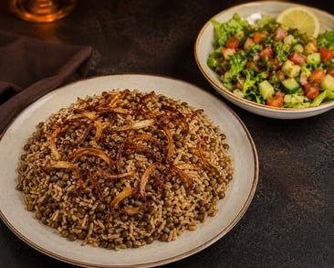 طبق مجدرة سورية بالعدس والأرز ومزين بالبصل المقلي، يقدم مع صحن سلطة خضراء طازجة.