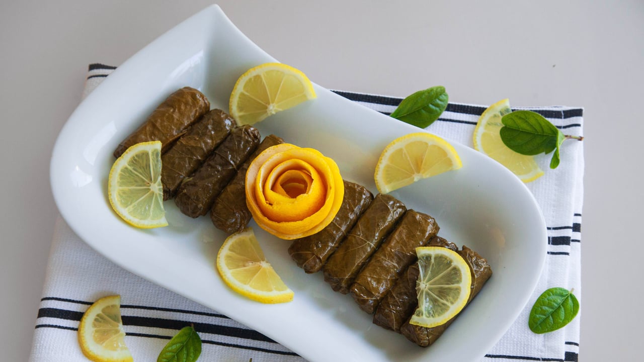 طبق ورق عنب محشي مع شريحة ليمون، وخلفه كوسا محشي وسلطة وزيت زيتون